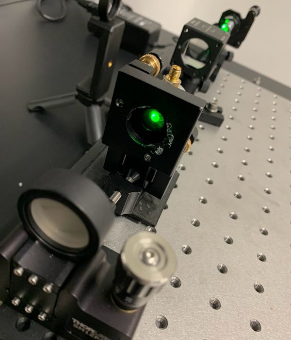 Close-up of a scientific apparatus with multiple components and a visible green laser.